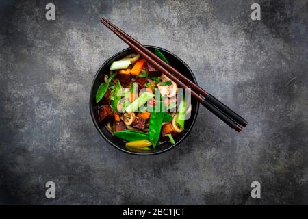 Ein Paar Essstäbchen und eine Schüssel mit verzehrfertiger Miso-Suppe mit udon-Nudeln, Tofu, Zuckererbsen, Paprika, Karotten, Mu-Err-Pilzen, Skalpell und Koriander Stockfoto