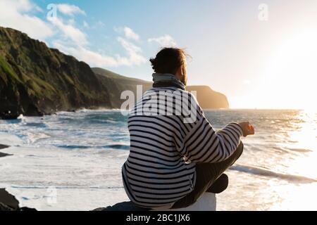 Mann meditiert an der Küste bei Sonnenuntergang, Sao Miguel Insel, Azoren, Portugal Stockfoto