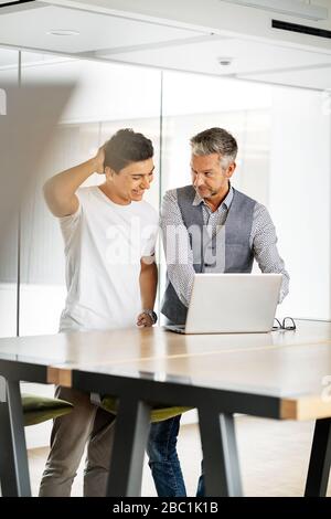 Leitender Geschäftsmann, der mit einem jungen Kollegen arbeitet und einen Laptop verwendet Stockfoto