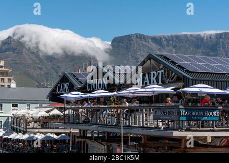 Kapstadt, Südafrika. 2019. Landcape Blick auf die Küste mit Touristen essen und trinken und Wolken schleichend über dem Gipfel des Tafelbergs. Stockfoto