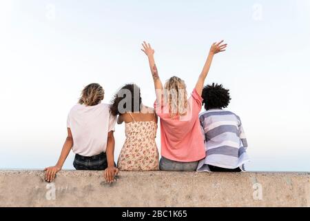 Rewr Ansicht von glücklichen Freunden sitzen auf einer Betonwand im Freien Stockfoto