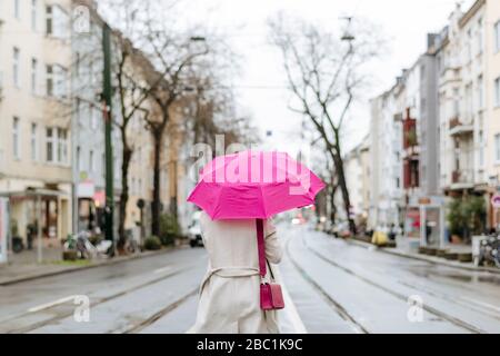 Rückansicht einer Frau mit rosa Regenschirm, die auf der Straße läuft Stockfoto