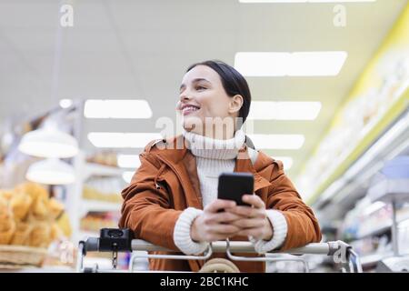 Lächelnde, selbstbewusste Frau mit Smartphone im Supermarkt einkaufen Stockfoto