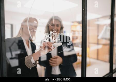 Reife und junge Geschäftsfrau Zeichnung Diagramm auf Glasscheibe im Büro Stockfoto