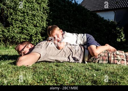 Porträt des barfuß kleinen Jungen auf dem Rücken seines Vaters im Garten entspannen Stockfoto