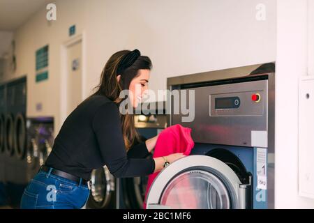 Junge Frau, die Wäsche in einem Waschsalon macht Stockfoto