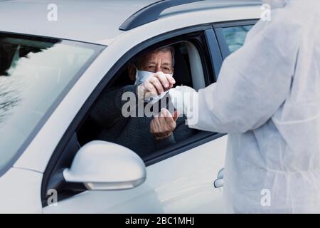 Mann, der Schutzkleidung trägt und den älteren Mann im Auto kontrolliert Stockfoto