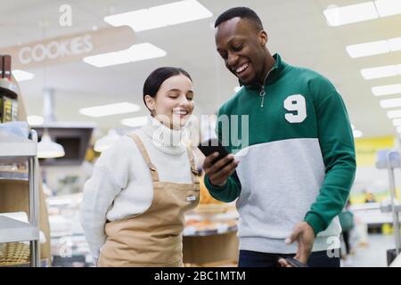 Lebensmittelhändler helfen Kunden mit Smartphone im Supermarkt Stockfoto