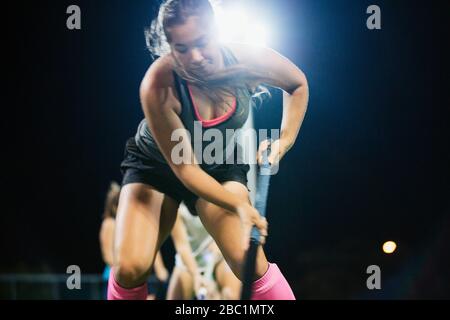 Entschlossener junger Feldhockeyspieler, der nachts Sportübung durchübt Stockfoto