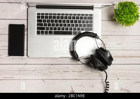 Laptop, leeres Handy und Kopfhörer auf rustikalem Holzhintergrund. Verspotten Sie sich mit leerem Smartphone-Bildschirm und Headset. Moderne Kopfhörer und Laptops Stockfoto