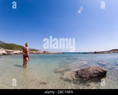 Rückblick auf die Frau in Bikini, die im seichten Meerwasser am Elafonissi Strand, Griechenland, steht Stockfoto