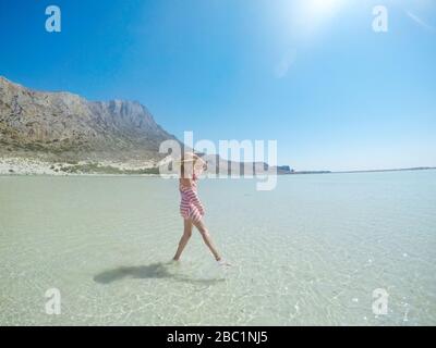 Fröhliche Frau, die im seichten Wasser im Meer spazieren geht. Sie befindet sich in türkisfarbenem Wasser am Balos Strand auf der Insel Crete. Stockfoto