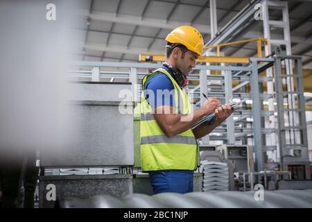 Männliche Führungskraft, die werkseitig in die Zwischenablage schreibt Stockfoto