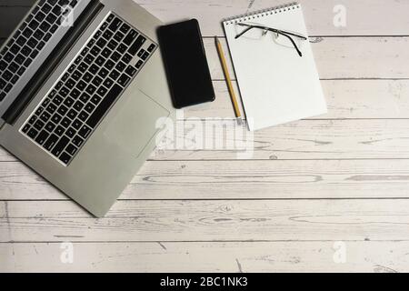 Laptop mit Smartphone, Brille, Notizblock und Bleistift auf leichtem Holztisch, Büromaterial Stockfoto