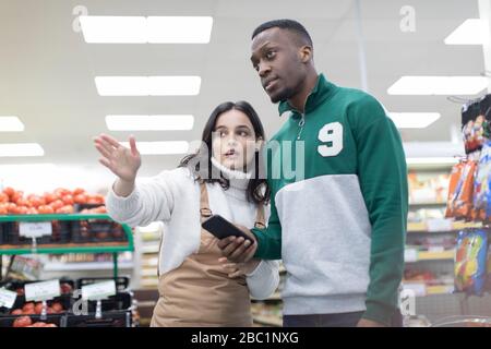 Weibliche Lebensmittelhändler helfen männlichen Kunden im Supermarkt Stockfoto