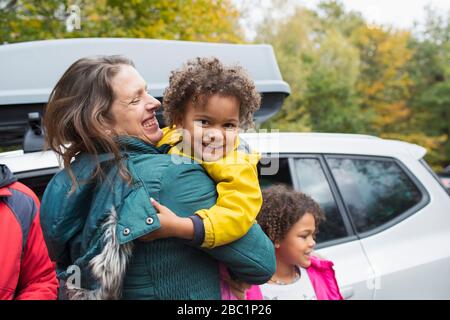 Portrait glückliche Mutter hält Tochter vor dem Auto auf dem Parkplatz Stockfoto