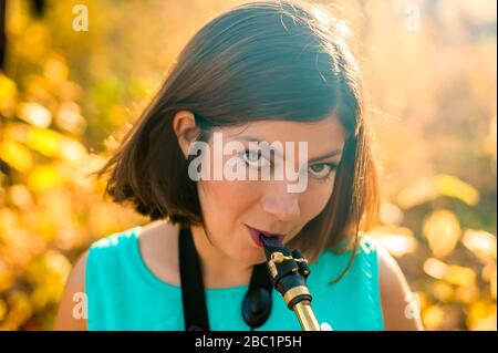 Porträt einer niedlichen jungen Saxophonistin mit schwarzen Haaren in blauer Kleidung auf gelbem Hintergrund Stockfoto