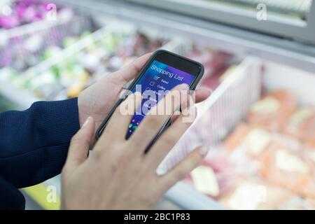 Nahaufnahme der Frau mit der App für die Einkaufsliste von Smartphones im Supermarkt Stockfoto