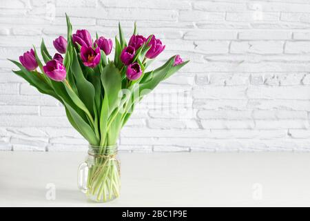 Wunderschöner Blumenstrauß aus violettem Tulpenblumen auf weißem Regal vor weißer Ziegelwand. Kopierbereich. Stockfoto