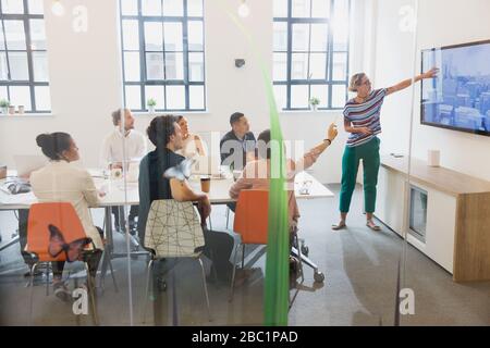 Weibliche Architektin auf Fernsehbildschirm führt Konferenzraum-Meeting Stockfoto