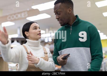 Weibliche Lebensmittelhändler helfen männlichen Kunden im Supermarkt Stockfoto