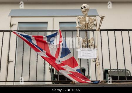 Southend-on-Sea, Großbritannien. April 2020. Ein Skelett, eine flagge des union Jack auf einem Balkon in der Nähe der Küste mit einem Warnschild für Coronavirus und soziale Distanzierung. Penelope Barritt/Alamy Live News Stockfoto