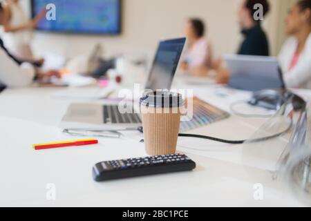 Einmal-Kaffeetasse und Fernbedienung auf dem Tisch in Konferenzräumen Stockfoto