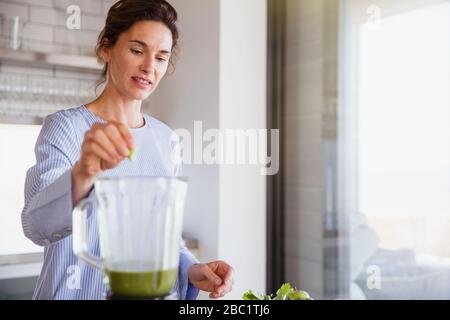 Frau, die in der Küche gesunden grünen Smoothie im Mixer zubereitet Stockfoto