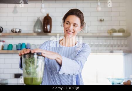 Lächelnde Frau, die in der Küche gesunden grünen Smoothie im Mixer zubereitet Stockfoto