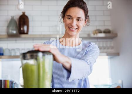 Lächelnde Frau, die in der Küche einen gesunden grünen Smoothie macht Stockfoto