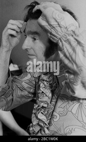 1970er Jahre, britischer Comedian und Entertainer von Kindern, Ken Goodwin, der Make-up vor einer Aufführung anwendet. Typischer 70er-Jahre-Look mit blumiger Hemd und langen Koteletten. Stockfoto