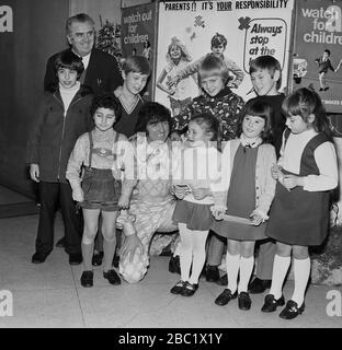 Der britische Comedian und Entertainer der Kinder, Ken Goodwin, mit einer Gruppe von Schulmädchen und Jungen vor Werbeplakaten für die Verkehrssicherheit von Kindern und dem Green Cross Code im Borough of Lewisham, South East London, England, Großbritannien. Stockfoto