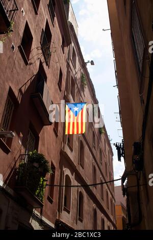 Blick auf die katalanische Flagge, die an der schmalen Straße und an historischen, alten Gebäuden im Viertel "Ciutat Vella" (gotisches Viertel) in Barcelona hing. Es ist eine sonnige Summe Stockfoto