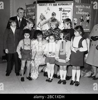 Der britische Comedian und Entertainer der Kinder, Ken Goodwin, mit einer Gruppe von Schulmädchen und Jungen vor Werbeplakaten für die Verkehrssicherheit von Kindern und dem Green Cross Code im Borough of Lewisham, South East London, England, Großbritannien. Stockfoto