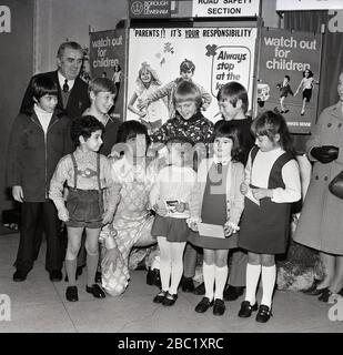 Der britische Comedian und Entertainer der Kinder, Ken Goodwin, mit einer Gruppe von Schulmädchen und Jungen vor Werbeplakaten für die Verkehrssicherheit von Kindern und dem Green Cross Code im Borough of Lewisham, South East London, England, Großbritannien. Stockfoto