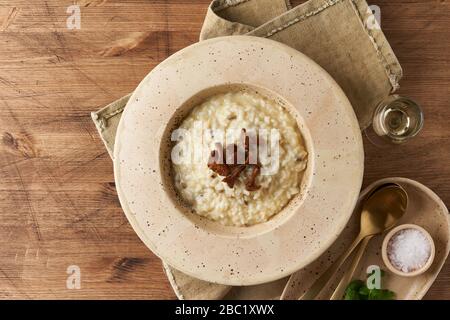 Risoto mit Chantellepilzen in großer Platte. Traditionelles italienisches Gericht. Alter Holztisch, Löffel, Serviette. Klassische heiße Gerichte aus Reis, Käse und WIN Stockfoto