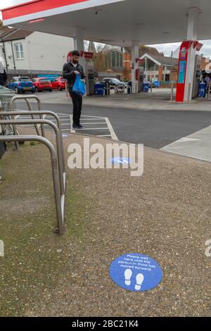 Southend-on-Sea, Großbritannien. April 2020. Kreisförmiges blaues Bodenschild, das die Einzelpersonen anweist, den Warteschlangenabstand beizubehalten. Mit weißem Text und Fußabdruckgrafiken Lesen Sie bitte hier, bis die Person vor Ihnen nach vorne gegangen ist. Dieses Bild auf einer strukturierten, kieseligen Oberfläche spiegelt Botschaften der öffentlichen Gesundheit während der COVID-19-Pandemie wider. Schilder auf dem Bürgersteig vor einem Supermarkt, die Kunden aufzeigen, wo sie stehen müssen, um eine sichere soziale Distanz zu wahren. Penelope Barritt/Alamy Live News Stockfoto