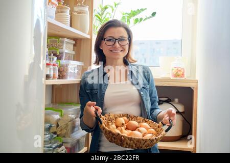 Frau in Pantry, die Korb mit Zwiebeln nimmt, Lebensmittelaufbewahrung in Pantry auf Holzregal Stockfoto