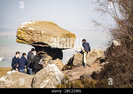 Eine Gruppe von Touristen stand neben der Steinsteinformation „The Druids Writing Desk“, Brimham Rocks, Harrogate, North Yorkshire, England, VEREINIGTES KÖNIGREICH. Stockfoto