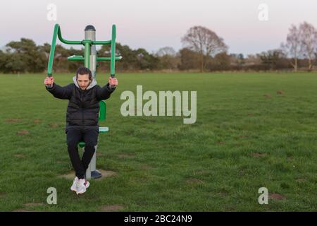 Ein junger Erwachsener, der in seinem örtlichen Park öffentliche Trainingsgeräte verwendet, um im Freien kostenlos zu trainieren Stockfoto