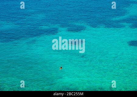Ein Mann schwimmt in das endlose kristallklare türkisfarbene Wasser der Vaporia-Region auf der griechischen Insel Syros, Kykladen, Griechenland Stockfoto
