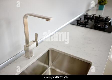 Modernes Design mit Chrom-Wasserhahn über Edelstahlwaschbecken auf der Tischplatte aus weißem Steinmarmor oder Granit. Stockfoto