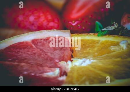 Makro-Nahaufnahme der halben Scheiben von rubinroten Grapefruit und Orange mit Erdbeeren im Hintergrund Stockfoto