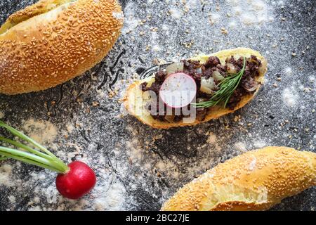 Maisbrot mit warmer Kaszanka (polnische Blutwurst), mit Zwiebel auf schwarzem Grund mit Mehl bestreut Stockfoto