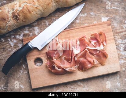 Spanischer Prosciutto, Baguette und Messer auf dem Tisch. Holztisch mit Mehl bestäubt Stockfoto