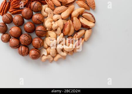 Verschiedene braune Nüsse auf grauem Grund. Macadami, Cashews, gehackte Mandeln, Pekannuss gesunde Nahrung Stockfoto