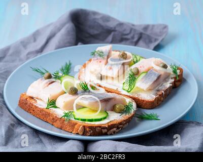 Hering Smorrebrod - traditionelle dänische Sandwiches. Schwarzes Roggenbrot mit Hering auf dunkelblau Stockfoto