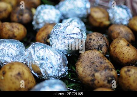Gebackene Kartoffeln in Aluminiumfolie zum Backen eingewickelt. Einige Kartoffeln ohne Folie. Stockfoto