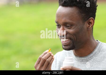 Portrait eines glücklichen schwarzen Mannes, der die Vitamin Omega3-Pille im Park nimmt Stockfoto