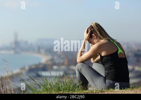 Frustrierte Läuferin sitzt im Freien und beschwert sich an einem sonnigen Tag in den Außenbezirken der Stadt Stockfoto